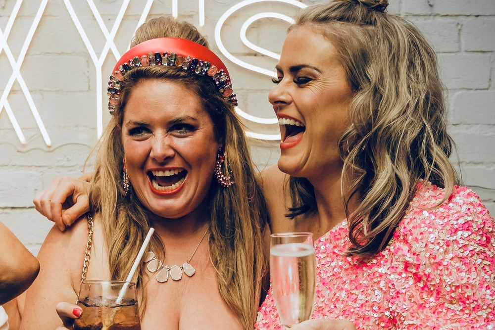 Two friends laughing with drinks in hand on a night out