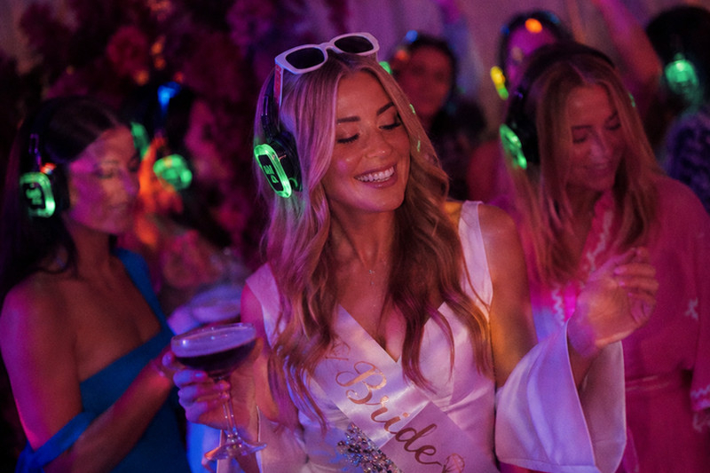 The bride in white and a sash dancing with glowing headphones on
