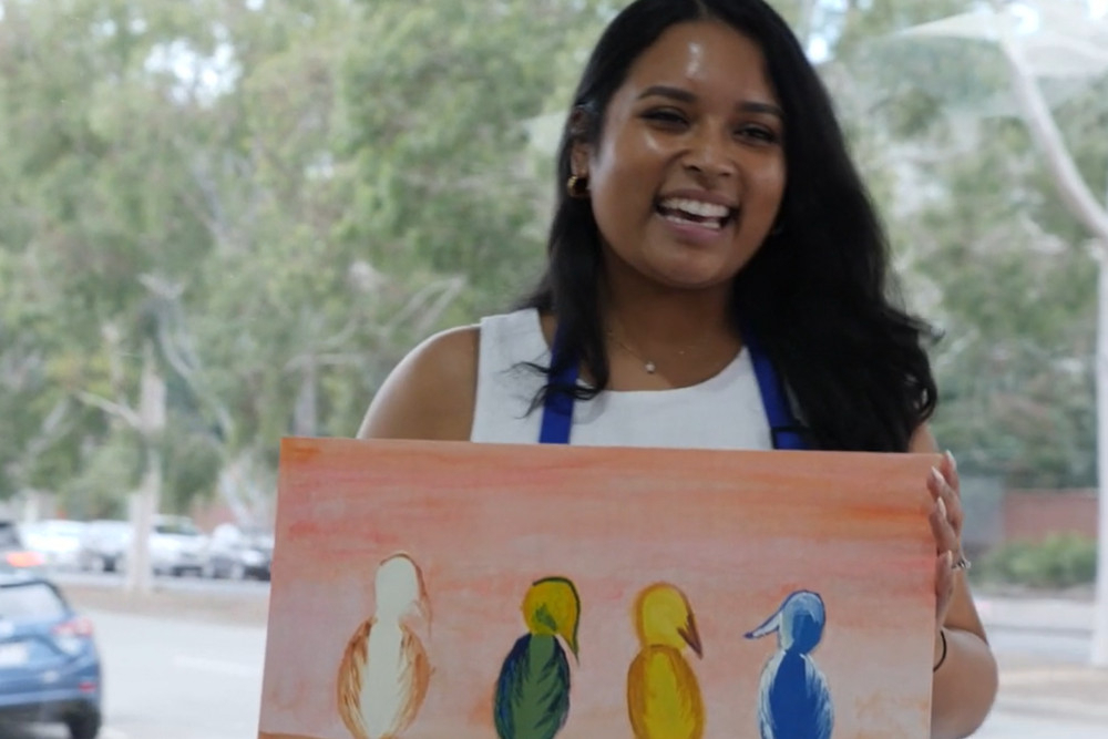 A laughing guest holding up her finished painting of four birds on a wire