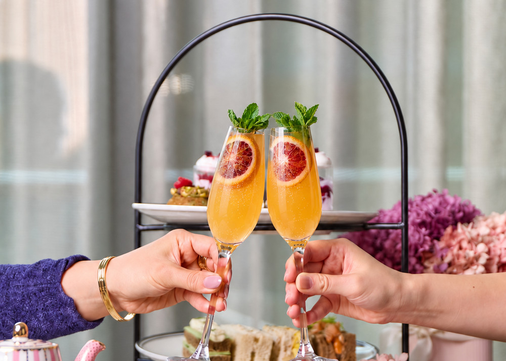 Two friends clinking glasses over a tiered high tea stand