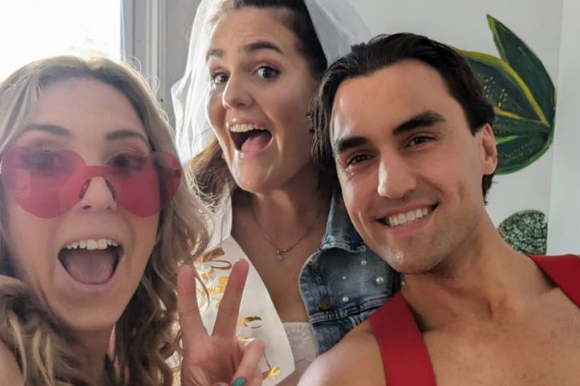 A selfie of two friends, one in a veil, with a shirtless fireman grinning behind them