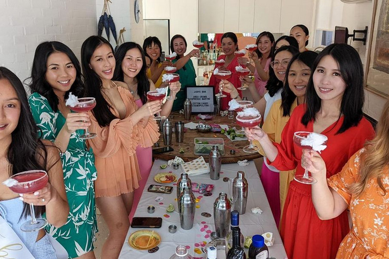 A big hens group raising pink cocktails along a table set with shakers and bottles