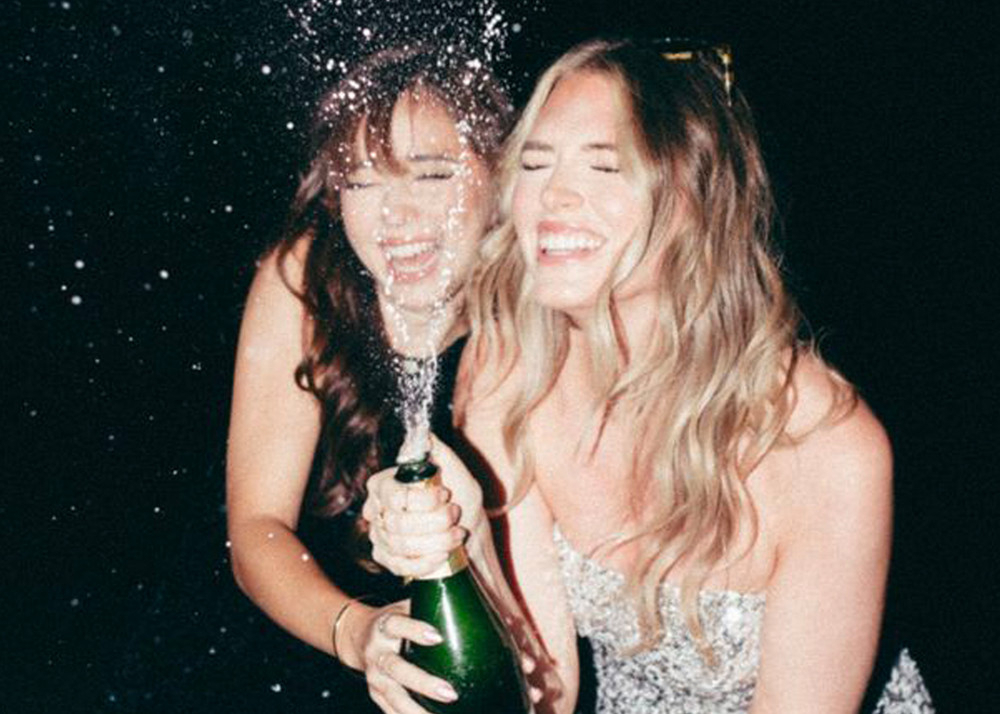 Two friends laughing as a bottle of bubbly sprays at night