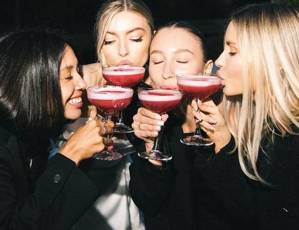 Four friends in black sipping red cocktails from coupe glasses together