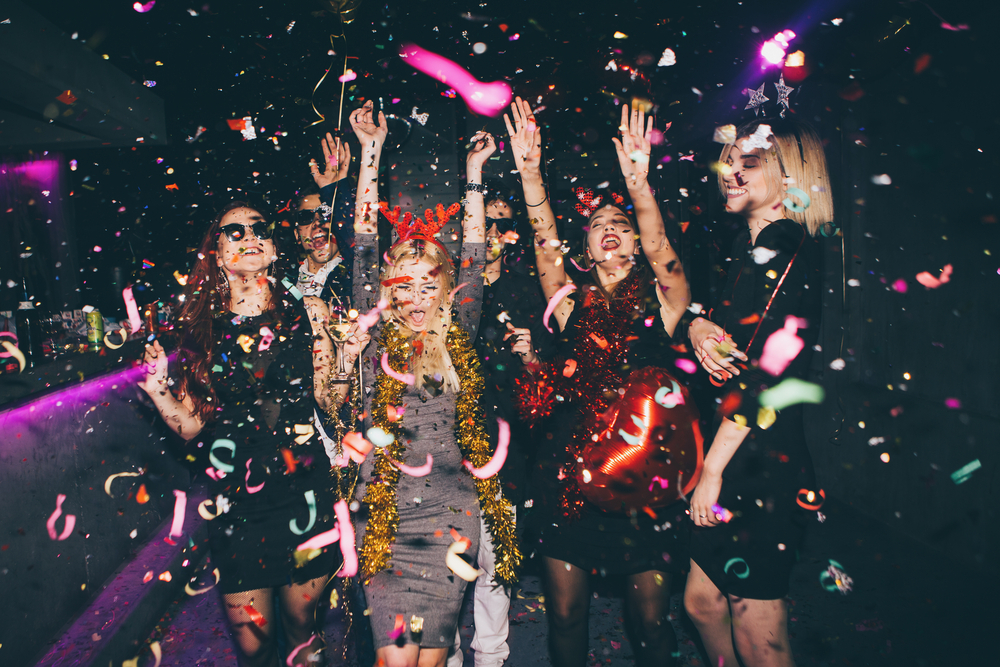 A group of friends dancing under falling confetti at a night party