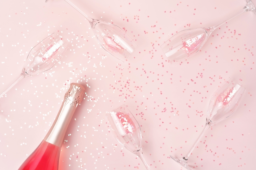 A bottle of pink bubbles and empty flutes scattered over pink confetti