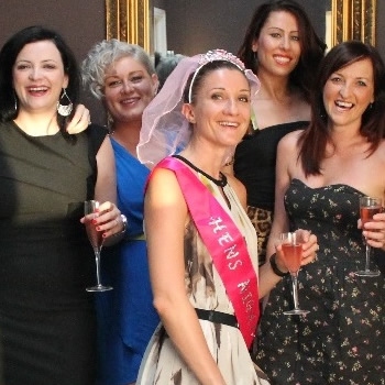 The bride in a pink sash and veil with her hens, glasses of rose in hand