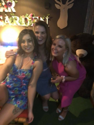 Three friends in colourful dresses smiling together on a couch at a bar