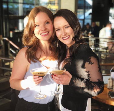 Two friends smiling with cocktails at the hens they celebrated