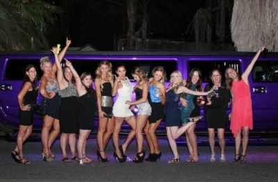The hens group lined up in front of a purple-lit hummer limo at night